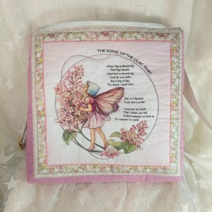 Könnte beinhalten: Eine rosa Stofftasche mit einem weißen Reißverschluss und einem Blumendesign. Die Tasche zeigt ein Gedicht über die Fliederfee und eine Illustration einer Fee mit Flügeln und einem Strauß Flieder.