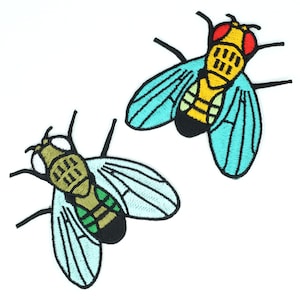 Könnte beinhalten: Zwei gestickte Bügeleisen-Aufnäher von Fliegen. Eine Fliege ist gelb mit roten Augen und die andere ist grün mit schwarzen Augen. Beide Fliegen haben blaue Flügel.