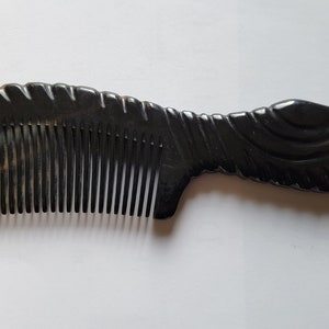 May include: A dark brown comb with a decorative handle. The comb's teeth are closely spaced, and the handle features a carved design. The comb has a smooth, polished finish and is made of a natural material.