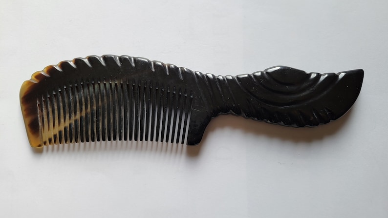 May include: A dark brown comb with a decorative handle. The comb's teeth are closely spaced, and the handle features a carved design. The comb has a smooth, polished finish and is made of a natural material.