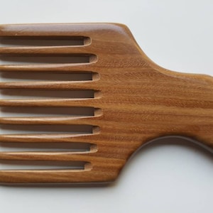 A wooden pick comb with a curved handle and nine teeth. The comb is made of light brown sandalwood with a natural grain pattern.