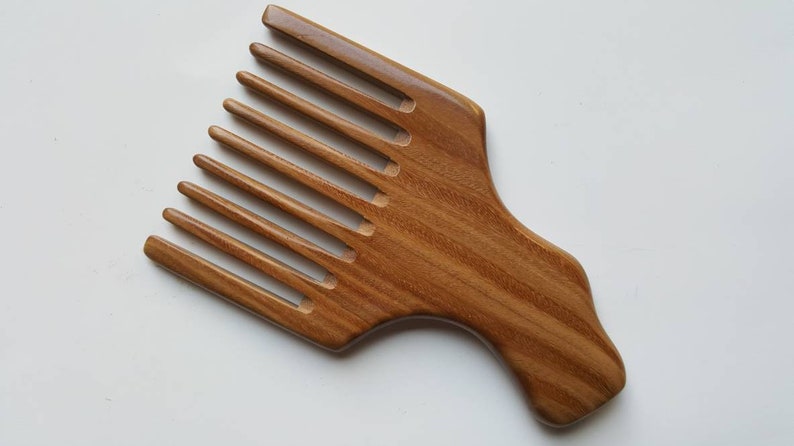 A wooden pick comb with a wide handle and a row of nicely spaced teeth. The comb is made of light brown wood with a natural grain pattern.
