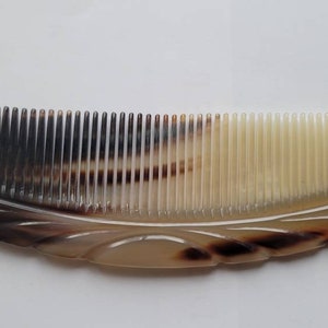 May include: A brown and cream colored comb with a curved shape and a decorative design. The comb has a fine tooth design.