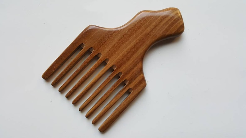 A wooden pick comb with a wide handle and multiple long teeth. The comb is made of light brown wood with a natural grain pattern.