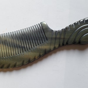 May include: A handcrafted comb with a dark gray and tan color scheme. The comb features closely spaced teeth and a decorative handle with a swirling design. The comb is made of a natural material.