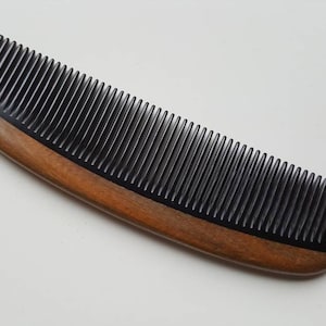 May include: A black comb with a wooden handle. The comb has fine teeth and is curved.