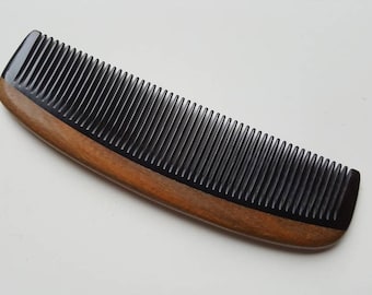 Pode incluir: Um pente preto com cabo de madeira. O pente tem dentes finos e é curvo.