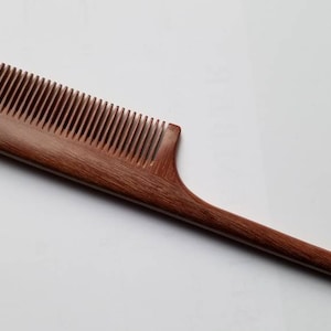 A long, wooden comb with a thin, pointed handle. The comb is made of dark brown wood with a natural grain pattern. Hand inlayed wood comb, sustainable gift