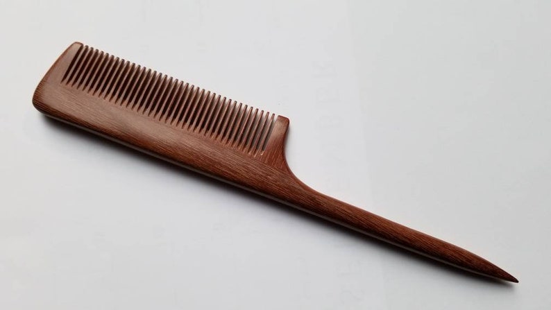 A long, wooden comb with a thin, pointed handle. The comb is made of dark brown wood with a natural grain pattern. Hand inlayed wood comb, sustainable gift