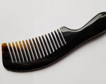 May include: A black comb with a curved handle and closely spaced teeth. The comb's teeth transition from light brown to black, and the handle is smooth and rounded. The comb is designed for hair care.