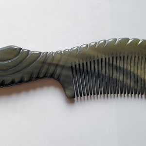 May include: A dark gray comb with a decorative handle and fine teeth. The comb has a curved design and is made of a smooth, polished material. The handle features carved details, and the teeth are evenly spaced.