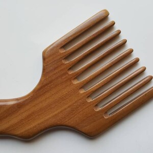 A sandalwood pick comb with a curved handle and nine teeth. The comb  has a smooth finish and comes with a fabric gift bag.  Gift for her!