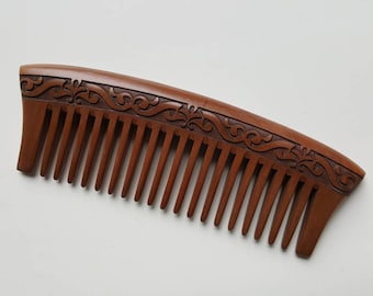 Pode incluir: Um pente de madeira castanho com um design floral esculpido. O pente tem um cabo curvo e é feito de madeira natural.