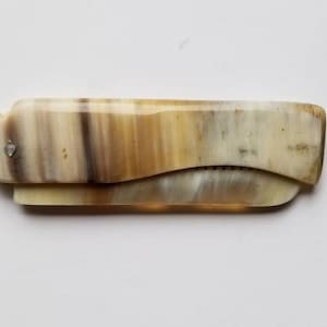 Könnte beinhalten: Ein kleiner, klappbarer Kamm aus braunem und weißem Horn. Der Kamm hat eine gebogene Form und einen silbernen Stift.