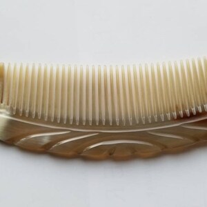 May include: A brown and white comb with a carved design. The comb is curved and has a wide tooth design.