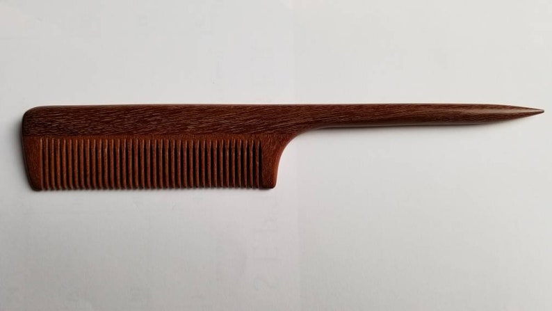 A rat tail wooden comb with a long, thin handle. The comb is brown and has a natural wood finish. Anti-static, Eco-friendly gift