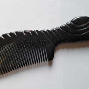May include: A handcrafted, dark brown comb with a decorative handle. The comb features a series of teeth and a handle with carved details. The handle has a curved, wing-like design. The comb's color transitions from a light brown to a dark brown.