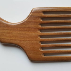 A wooden pick comb with a unique handle design. The comb has nine teeth and is made of light brown sandalwood.  Gift for him who grows long hair!