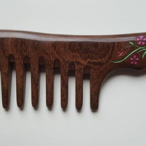 A dark brown wooden comb with a floral design on the handle. The flowers vase design is in impressionist style.