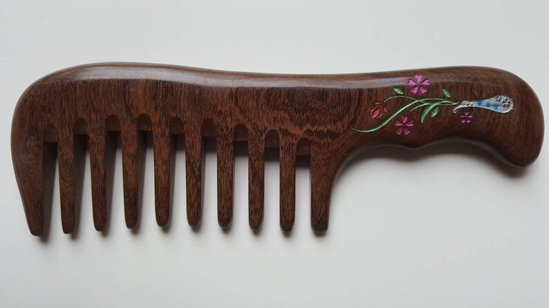 A dark brown wooden comb with a floral design on the handle. The flowers vase design is in impressionist style.