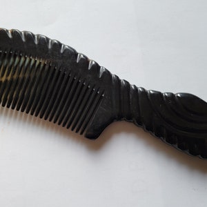 May include: A dark brown comb with a curved handle and fine teeth. The comb has a decorative, carved handle and a lighter brown tip. The comb is made of a smooth, polished material.