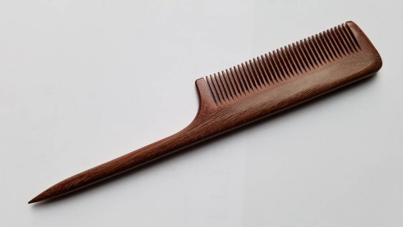 A long, thin, wooden comb with a pointed handle. The comb is made of dark brown pau rosa wood and has fine teeth.  it is designed for precision sectioning and hair styling.