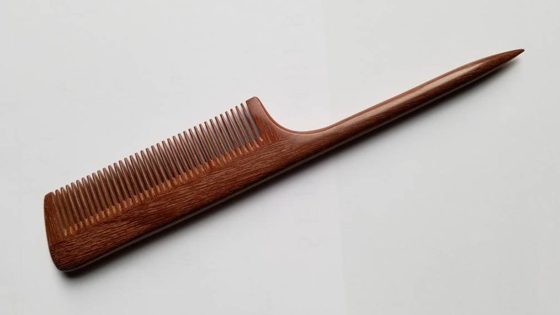 A brown wooden comb with a long, thin handle. The comb has a rounded edge and a pointed tip.