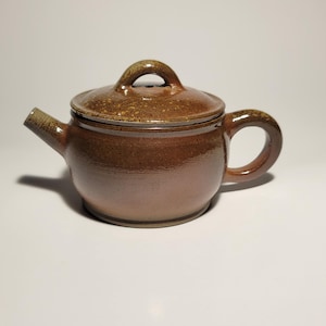 以下が含まれることがあります： 茶色の陶器のティーポットと、お揃いの蓋。 ティーポットは丸みを帯びたボディ、湾曲したハンドル、注ぎ口を備えています。 蓋には小さなループハンドルが付いています。 ティーポットは光沢のある仕上げです。