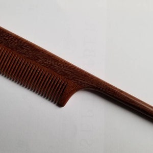 A long, thin, wooden comb with a dark brown color and a fine-toothed comb on one end. The comb has a long, thin handle.