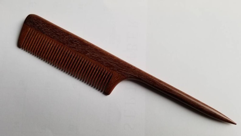 A long, thin, wooden comb with a dark brown color and a fine-toothed comb on one end. The comb has a long, thin handle.