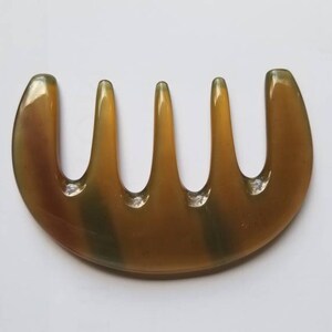 A brown, semi-circular comb with five tines and a smooth, polished finish. The comb has a natural, earthy color with subtle variations. The design is simple and functional, suitable for hair care.