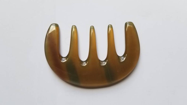 A brown, semi-circular comb with five tines and a smooth, polished finish. The comb has a natural, earthy color with subtle variations. The design is simple and functional, suitable for hair care.