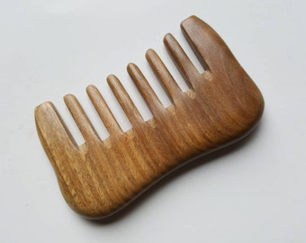 Könnte beinhalten: Ein Holzkamm mit natürlicher brauner Oberfläche und einer geschwungenen Form. Der Kamm hat neun Zähne.