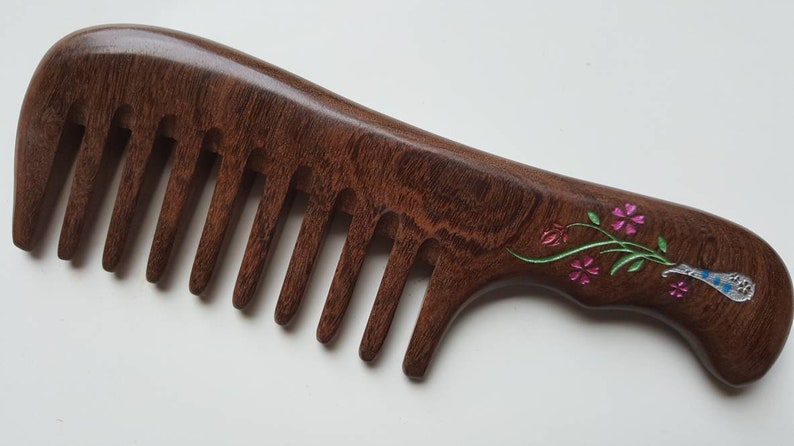A dark brown wooden comb with a floral design on the handle. The flowers are pink and green, and the handle has a silver-colored accent.