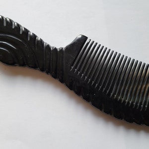 May include: A dark, horn comb with a decorative handle. The comb features a series of closely spaced teeth and a curved handle with carved details. The comb's color is a deep black with a hint of brown at the base.