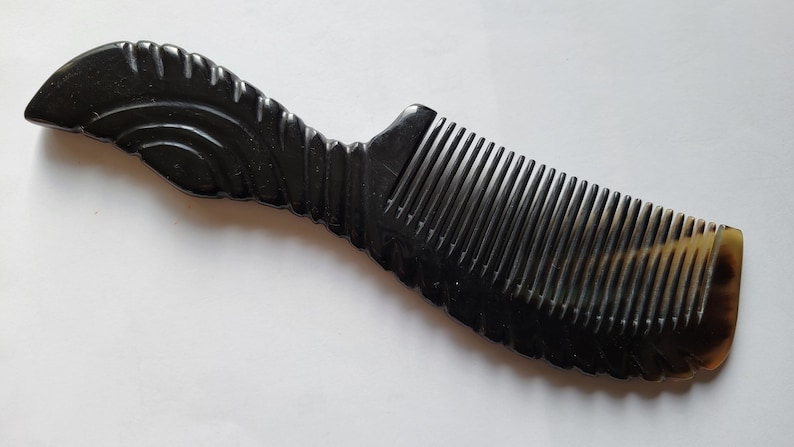 May include: A dark, horn comb with a decorative handle. The comb features a series of closely spaced teeth and a curved handle with carved details. The comb's color is a deep black with a hint of brown at the base.