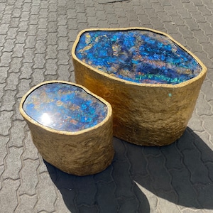 May include: Two round side tables with blue, iridescent, glass tops, finished in gold leaf. The larger table is in the background and the smaller table is in the foreground.