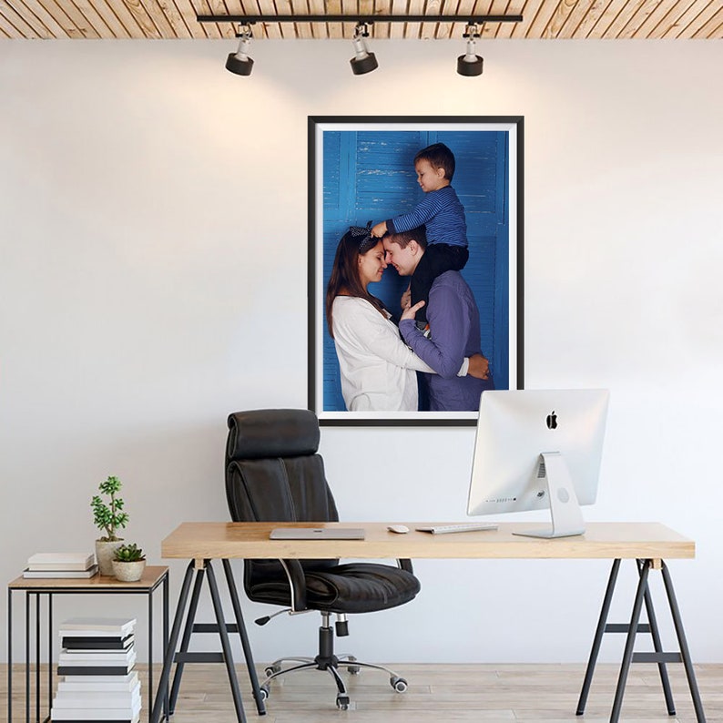 K&ouml;nnte beinhalten: Ein gerahmtes Foto einer Familie, bestehend aus einem Mann, einer Frau und einem Kind. Die Familie umarmt sich, wobei das Kind auf den Schultern des Mannes sitzt. Das Foto befindet sich in einem schwarzen Rahmen und h&auml;ngt an einer wei&szlig;en Wand.