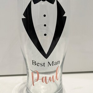 May include: A clear glass pint glass with a black tuxedo design and the text "Best Man Paul" in rose gold lettering.