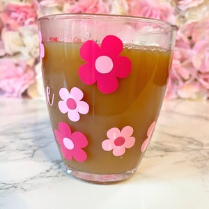 May include: A clear glass mug with a brown beverage inside. The mug has pink and white flower decals on the outside.