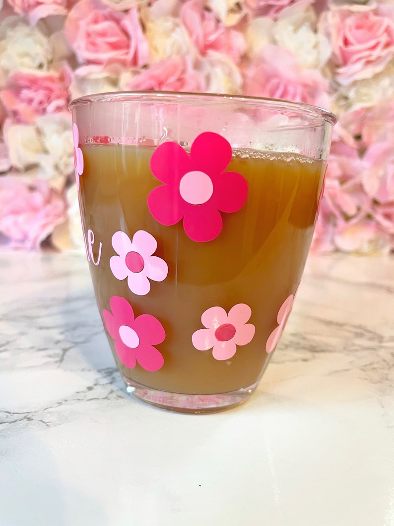 May include: A clear glass mug with a brown beverage inside. The mug has pink and white flower decals on the outside.