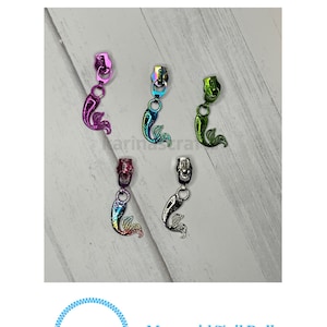 May include: Five zipper pulls with mermaid tail designs in various colors, including pink, green, blue, and silver. The zipper pulls are on a white wooden surface. The text "Karinas Crafts" and "Mermaid Tail Pull" is visible below the zipper pulls.