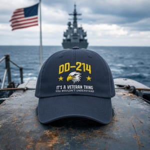 May include: Navy blue baseball cap with the text "DD-214" in yellow, an eagle graphic, and the phrase "It's a Veteran Thing You Wouldn't Understand." An American flag waves in the background.