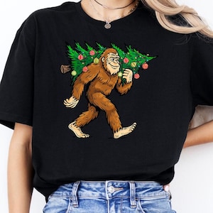Bigfoot Carrying Christmas Tree Shirt, Sasquatch Tee, Xmas Tree Light Shirt, Holiday Fun Tee, Gift for Bigfoot Lover, Festive Sasquatch Tee