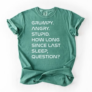 May include: Light green t-shirt with the text "GRUMPY. ANGRY. STUPID. HOW LONG SINCE LAST SLEEP, QUESTION?" in white. The shirt is folded at the bottom and has rolled-up sleeves. The words "Light green" are in the bottom right corner.
