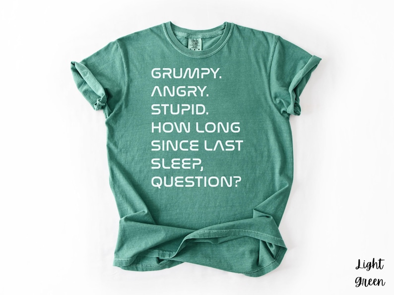 May include: Light green t-shirt with the text "GRUMPY. ANGRY. STUPID. HOW LONG SINCE LAST SLEEP, QUESTION?" in white. The shirt is folded at the bottom and has rolled-up sleeves. The words "Light green" are in the bottom right corner.