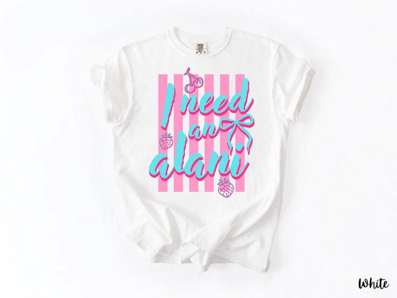 May include: A white short-sleeved t-shirt featuring a graphic design with vertical pink stripes. The text "I need an alani" is printed in a bright blue script font, accompanied by illustrations of cherries, a bow, and two strawberries.