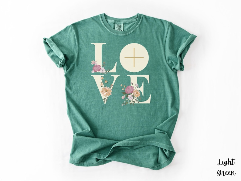 May include: A light green t-shirt featuring the word "LOVE" in a cream font. The "O" is a circle with a cross, and the letters "L" and "V" are decorated with flowers. The words "Light green" are in the bottom right corner.