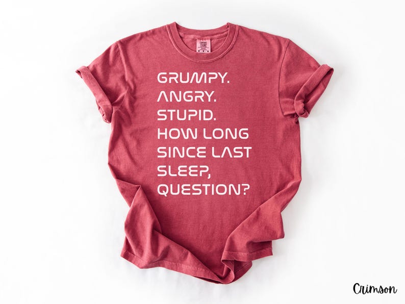 May include: Crimson-colored t-shirt with the text "GRUMPY. ANGRY. STUPID. HOW LONG SINCE LAST SLEEP, QUESTION?" in white block letters. The shirt has rolled-up sleeves and a crew neck.