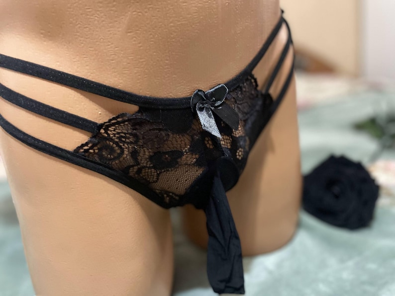 K&ouml;nnte beinhalten: Schwarze Spitzenunterw&auml;sche mit Schleifendetail und Riemen-Design. Die Unterw&auml;sche ist aus durchsichtigem Stoff und hat ein zartes Spitzenmuster.